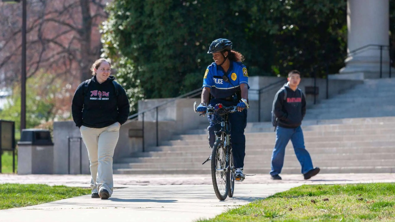 photo of campus police riding a bike alongside a UMD student by John Consoli