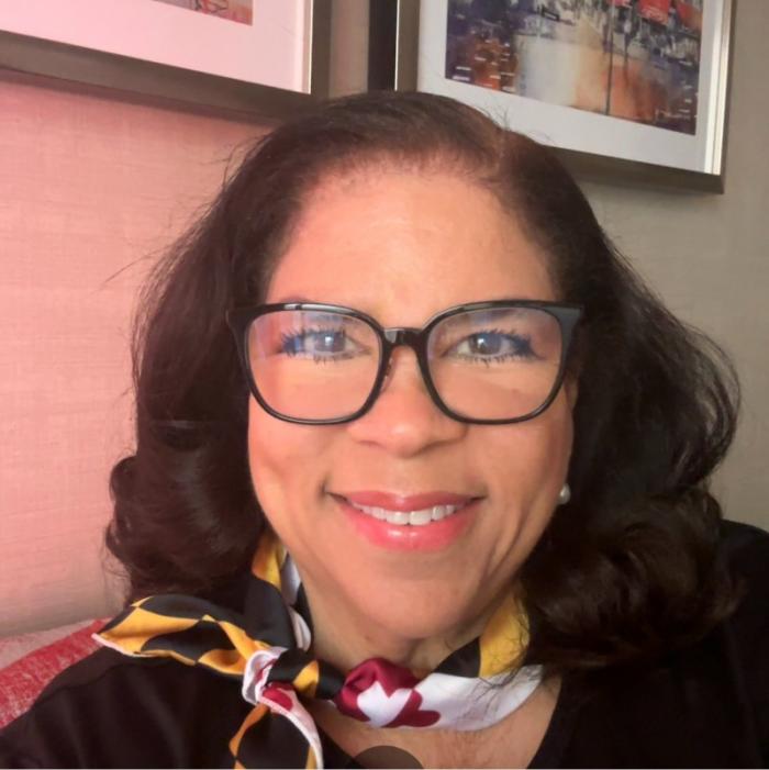 headshot photo of Kim Rice DeGross, who has short, dark hair, glasses, and is wearing a Maryland flag scarf