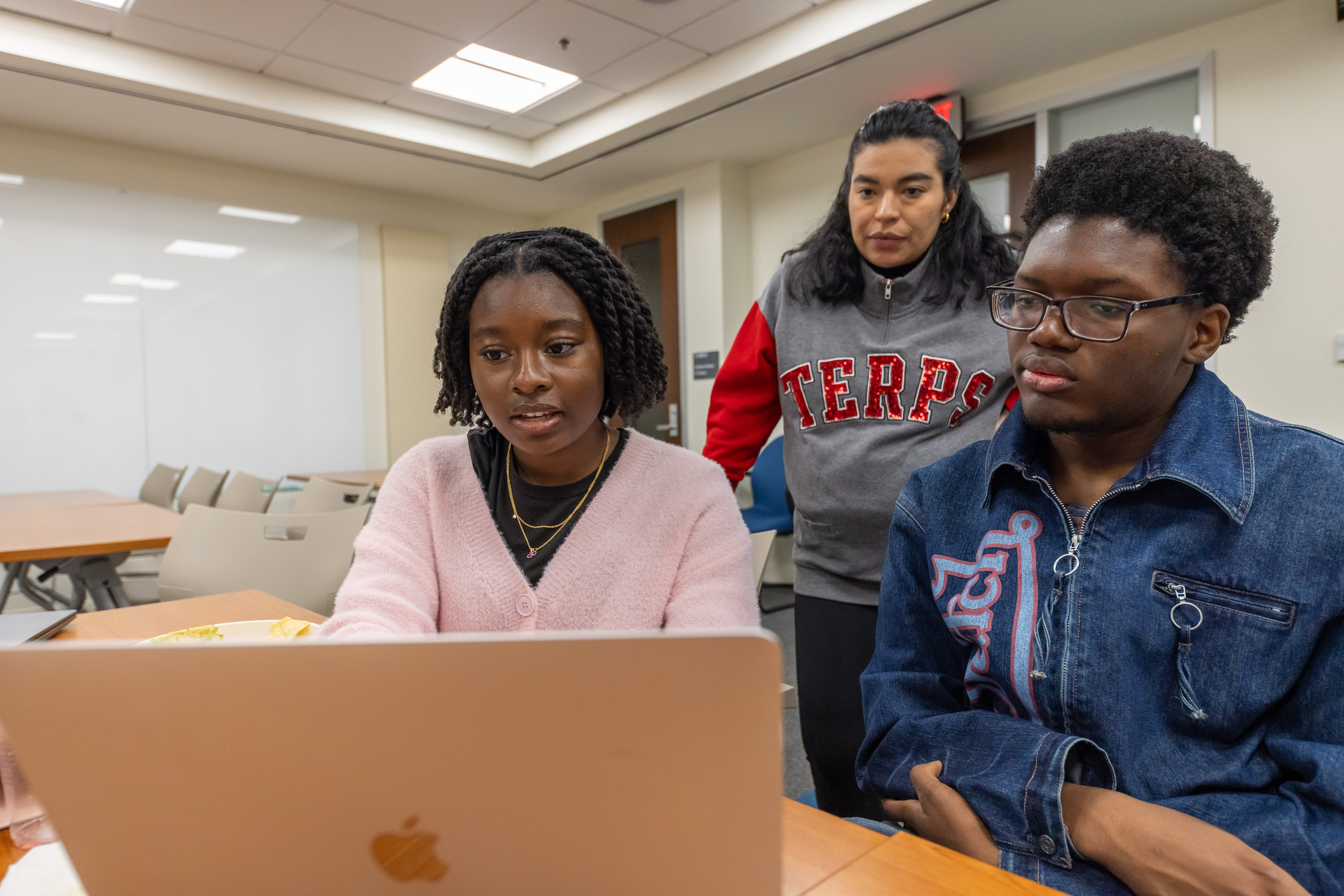 Photo of two students in the Black Youth Happiness Movement Internship looking at a computer with a research assistant standing behind them