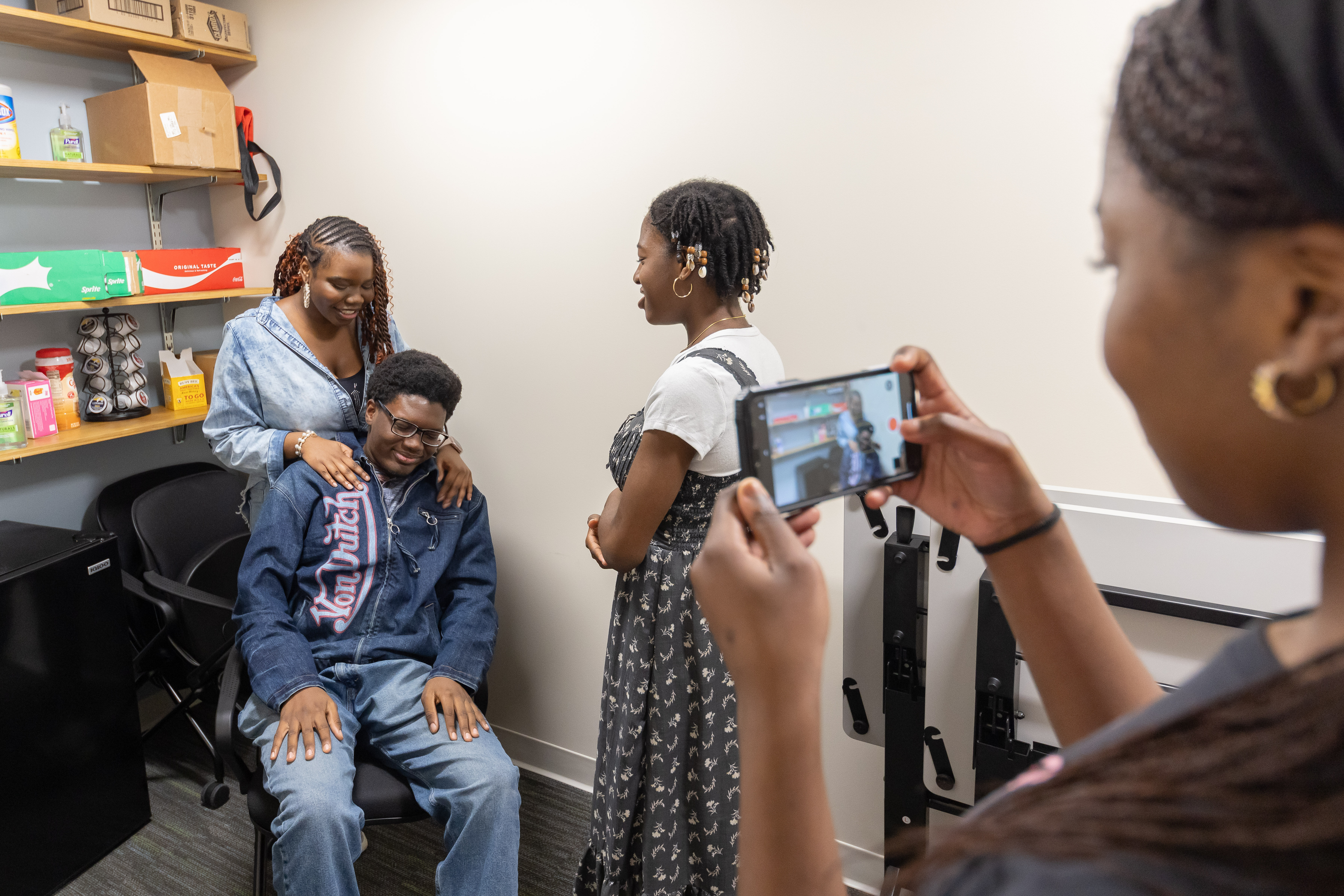 Photo of three students in the Black Youth Happiness Movement  acting in a video advertisement for their app, VIBE, with a fourth student recording them on her phone
