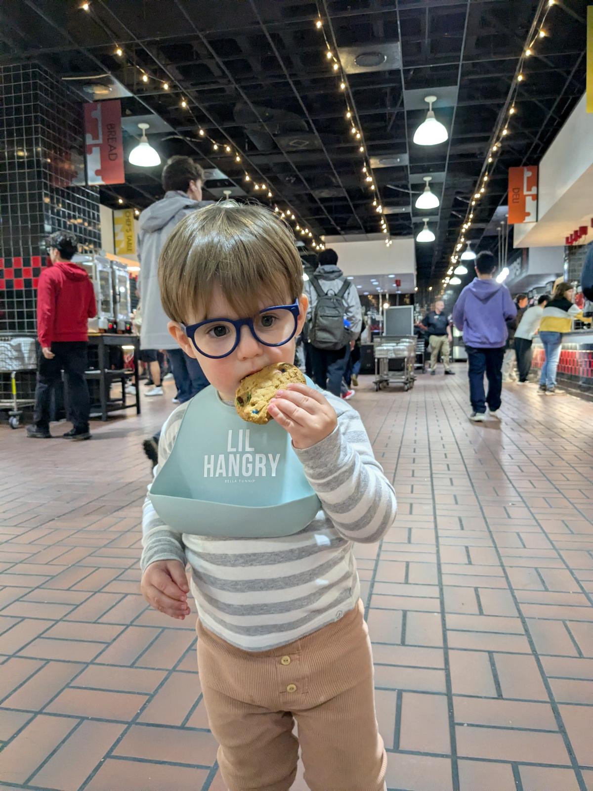 LEAP student Adrien wearing a bib that says LITTLE HANGRY and eating a chocolate chip cookie at the UMD South Campus Dining Hall