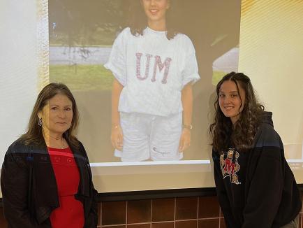 professor nan ratner and student peyton wilkie posing in front of a projected photo of peyton's mother, who was also a student of Professor Ratner's