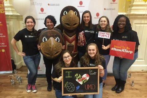 Ambassadors and Testudo smiling in front of UMD backdrop.