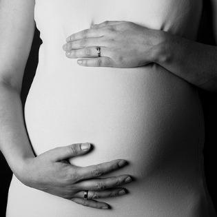 A pregnant woman puts her hands on her abdomen.