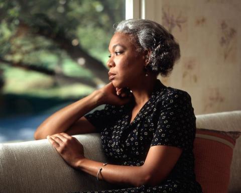 An older black woman looks out a window.